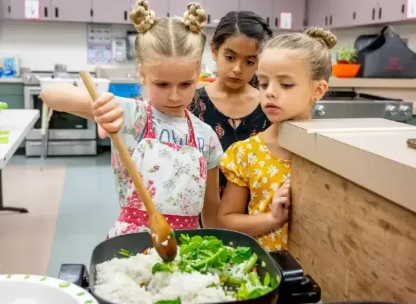 A group of young girls are cooking food in a kitchen.
