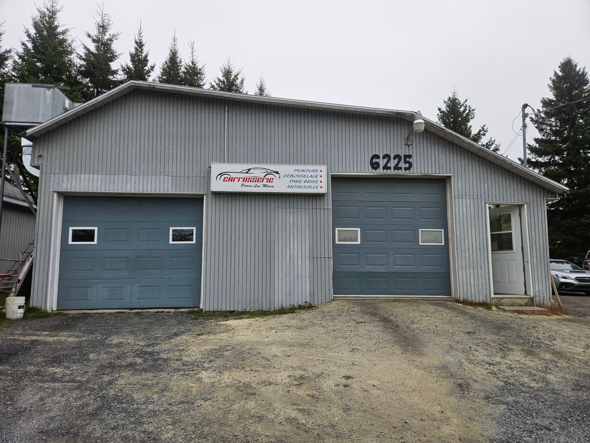 Bâtiment gris avec deux portes de garage et une enseigne pour la réparation automobile, adresse 6225.