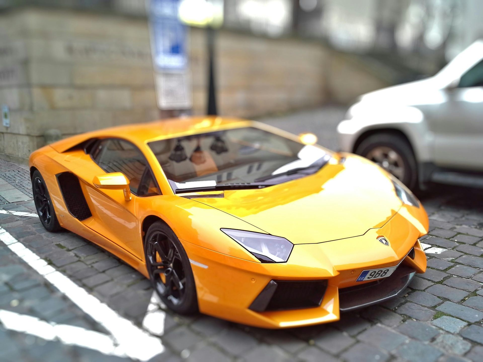 Une Lamborghini jaune, voiture de sport, est garée dans une rue pavée, à côté d'un SUV blanc.