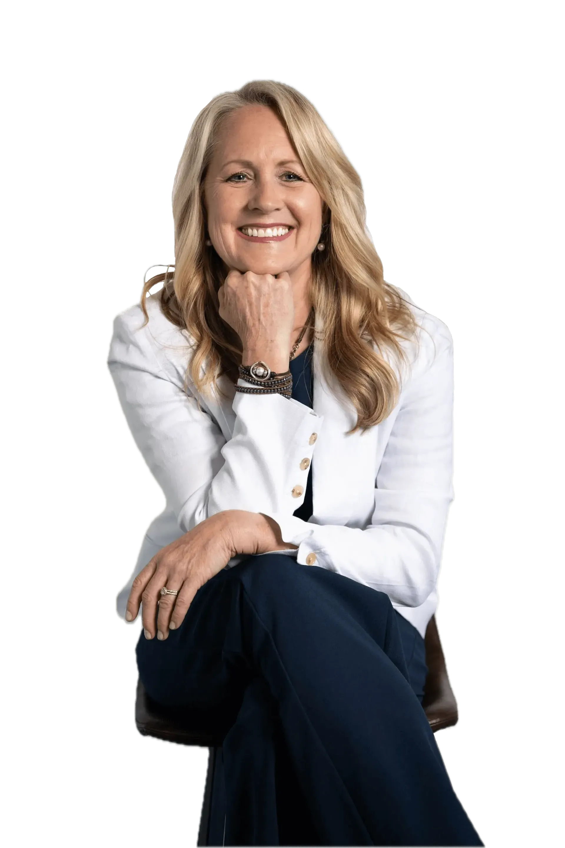 Smiling woman in a white blouse and dark pants, seated with her chin resting on her hand.