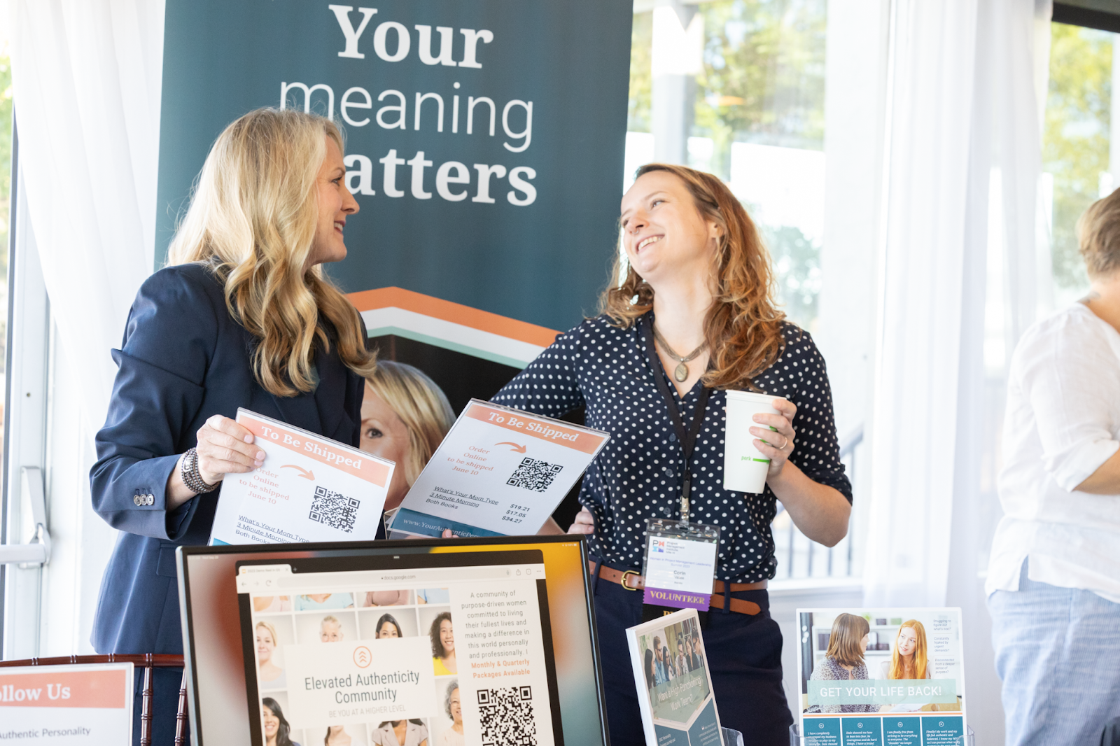 Two women chatting at a booth with flyers and a sign reading “Your meaning matters”
