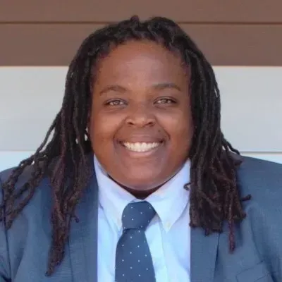 Smiling person in a blue suit and tie against a striped background