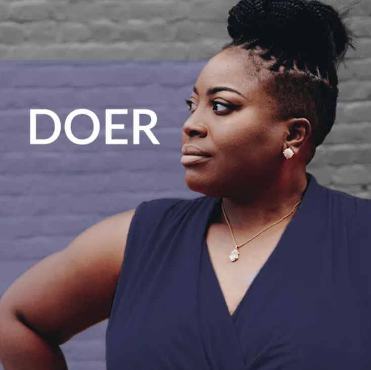 Woman in navy dress with word “DOER” beside her on a purple brick wall background