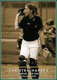 Softball catcher in black jersey and white pants, holding a mitt and calling out on the field.