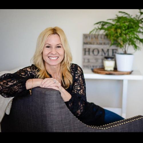 Smiling woman in a black lace top leaning on a dark chair in a bright living room
