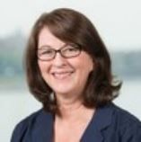 Portrait of a smiling woman with shoulder-length brown hair and glasses, wearing a blue top against a light background