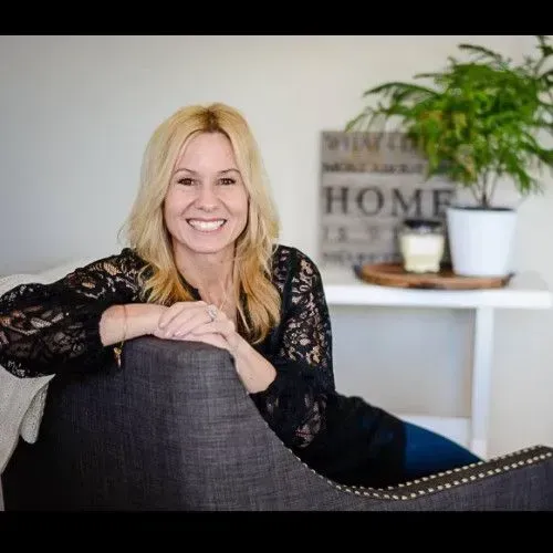 Smiling woman leaning on a gray chair in a bright living room with a plant and home decor in the background