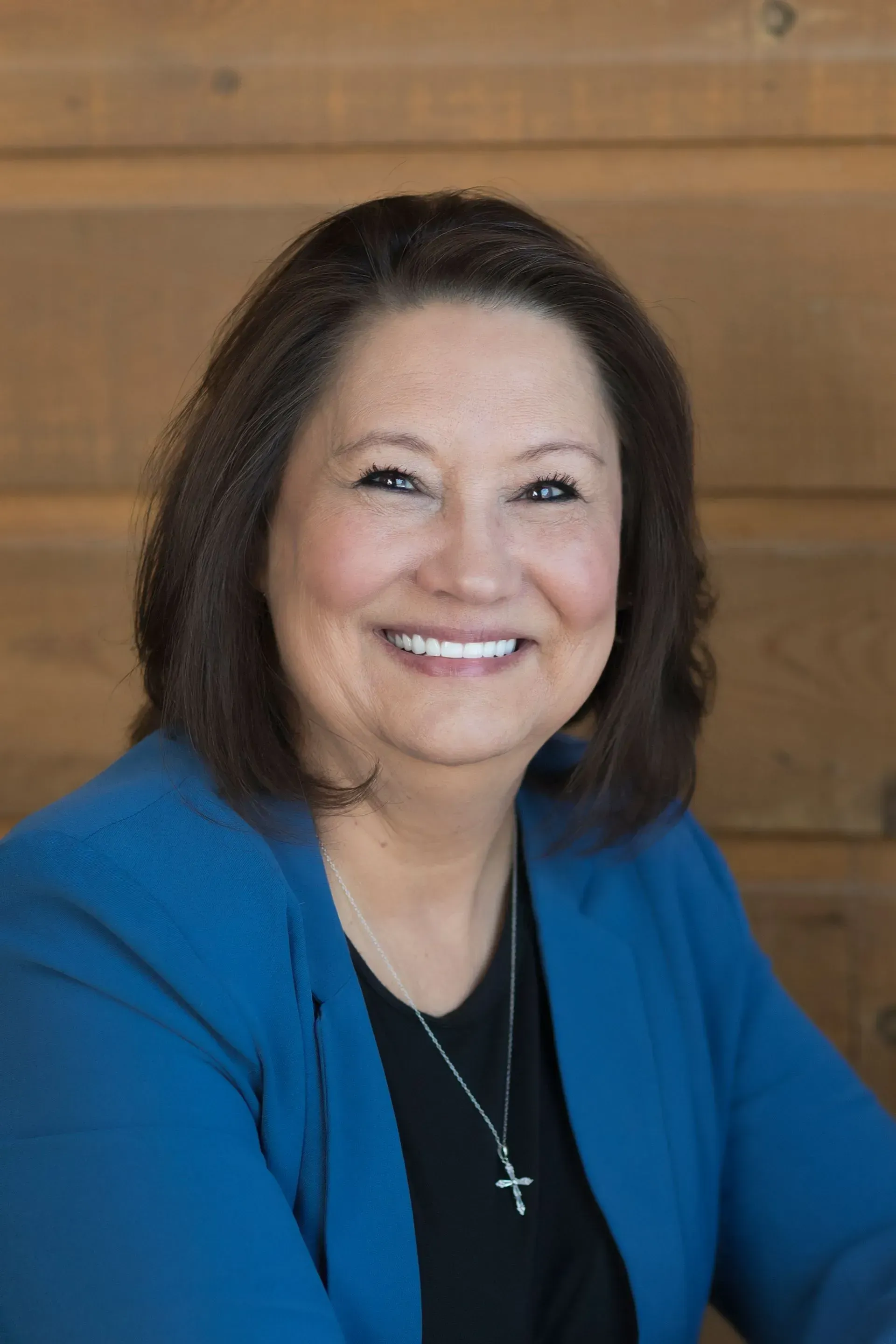 Smiling woman in a blue blazer and black top against a wooden background.