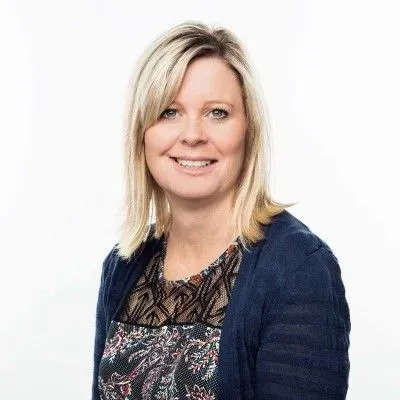 Smiling blonde woman in a navy cardigan and patterned blouse on a white background