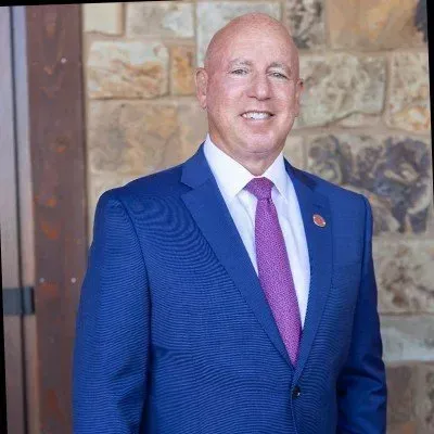 Man in a blue suit and pink tie smiling in front of a stone wall