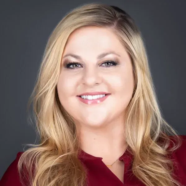 Smiling blonde woman in a burgundy blouse against a dark gray background