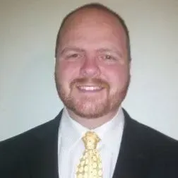 Smiling man in a dark suit, white shirt, and yellow tie against a plain background