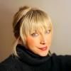 Portrait of a blonde person in a black turtleneck against a dark background