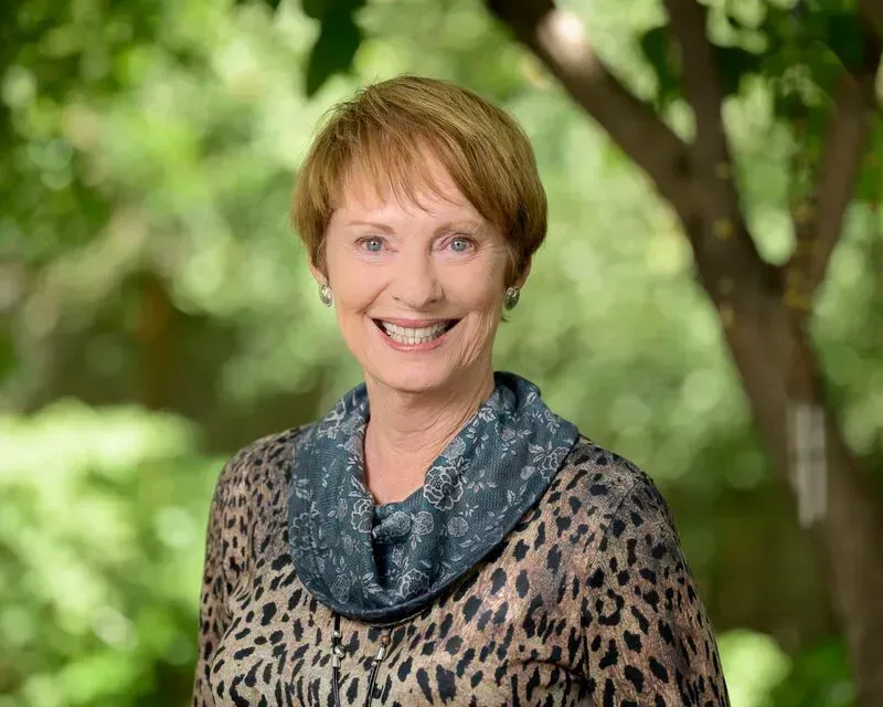 Smiling woman in a leopard-print top and blue scarf, standing outdoors with a blurred green background