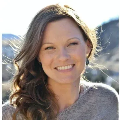 Smiling woman outdoors in sunlight, with mountains blurred in the background