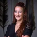 Smiling person with curly hair in a black top, seated against a gray background