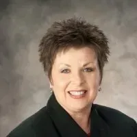 Smiling person with short spiky hair in a dark blazer against a gray studio backdrop