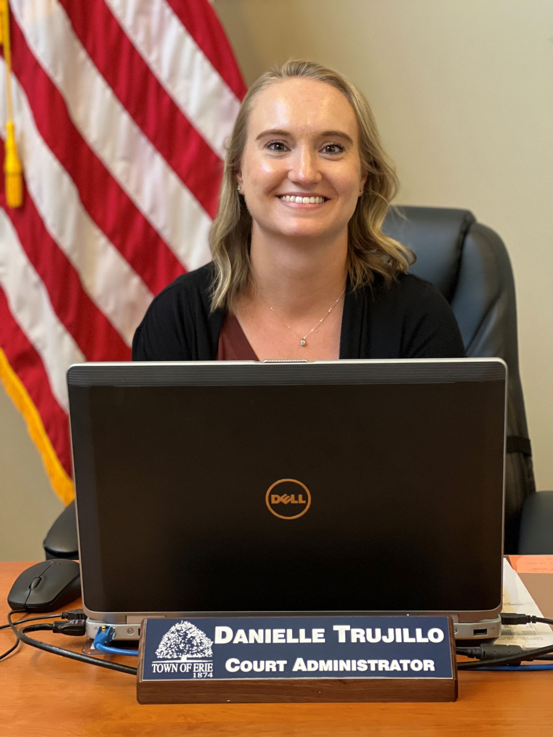 Woman seated at a desk behind a Dell laptop with a U.S. flag in the background