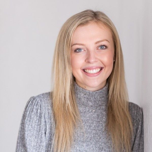 Portrait of a smiling blonde woman in a gray sweater against a light background
