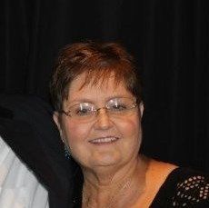 Smiling woman with short brown hair and glasses against a dark background