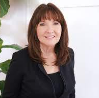 Smiling woman in a black blazer standing indoors against a light background