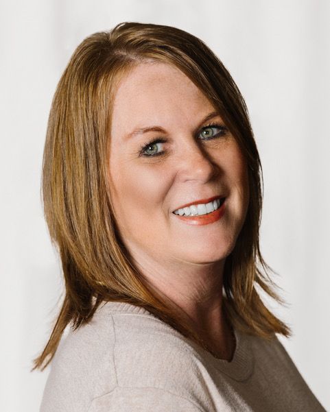Smiling woman with shoulder-length blonde hair against a light background