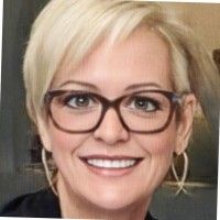 Smiling blonde person wearing black glasses and hoop earrings against a neutral background