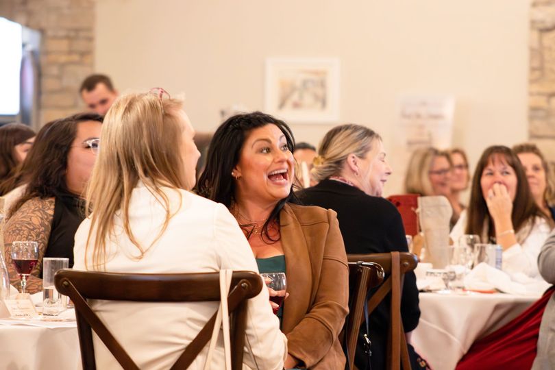 Guests seated at tables in a bright banquet hall, chatting and smiling during an event