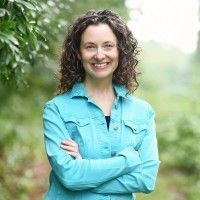 Smiling person in a turquoise shirt standing outdoors with arms crossed