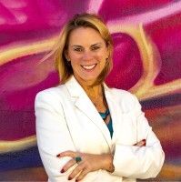 Smiling woman in a white blazer standing with arms crossed before a colorful abstract backdrop