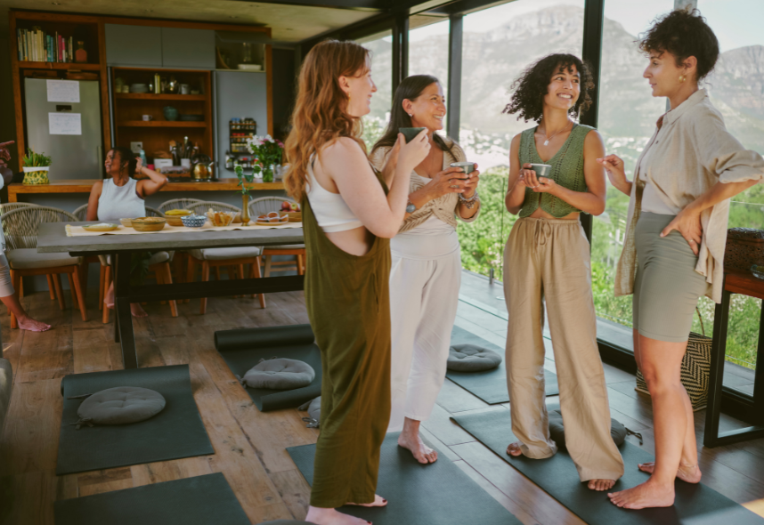 Four people chatting in a bright modern living room with large windows and low floor cushions.