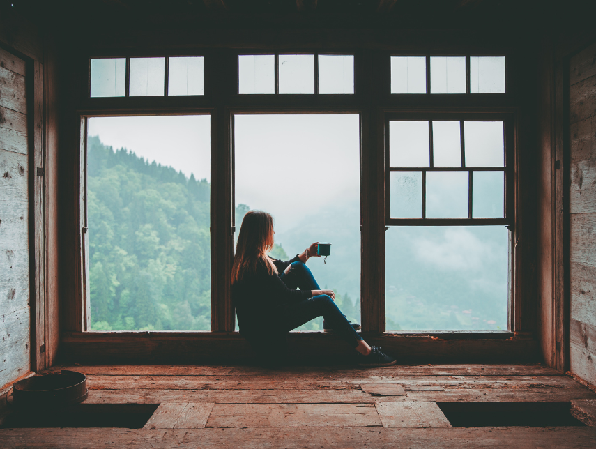 Silhouette of a person sitting by a large window, reading with mountains visible outside