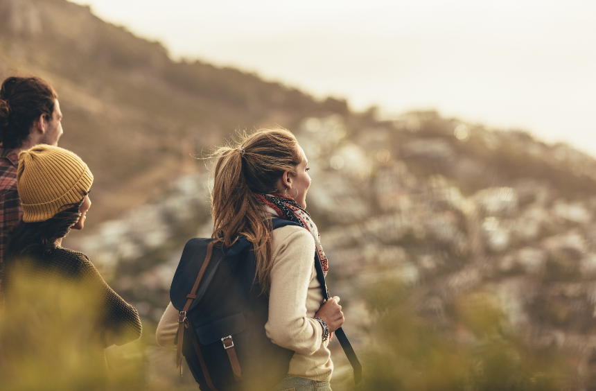Two hikers with backpacks overlooking a blurred hillside town at sunset