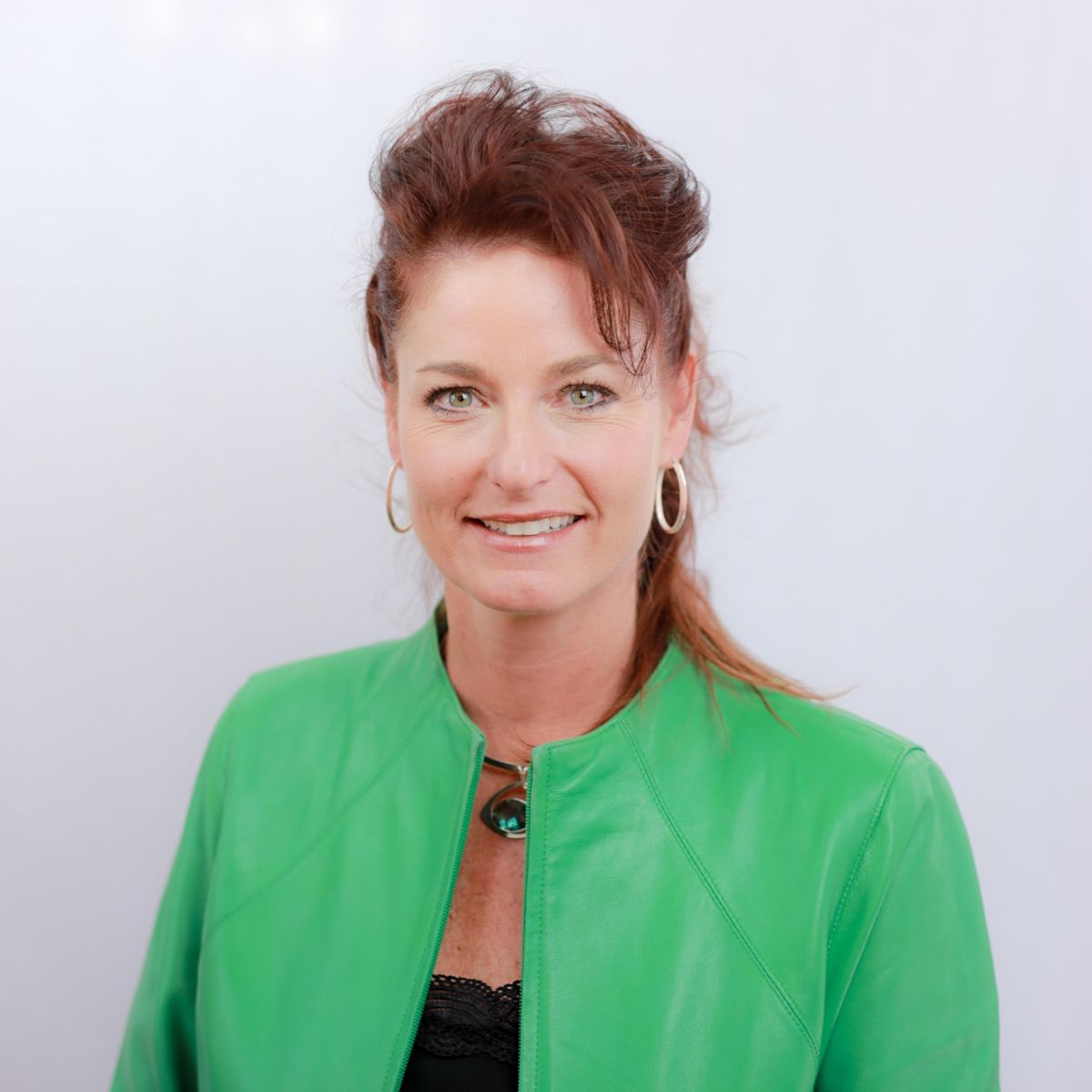 Woman in a bright green jacket smiling against a plain light background