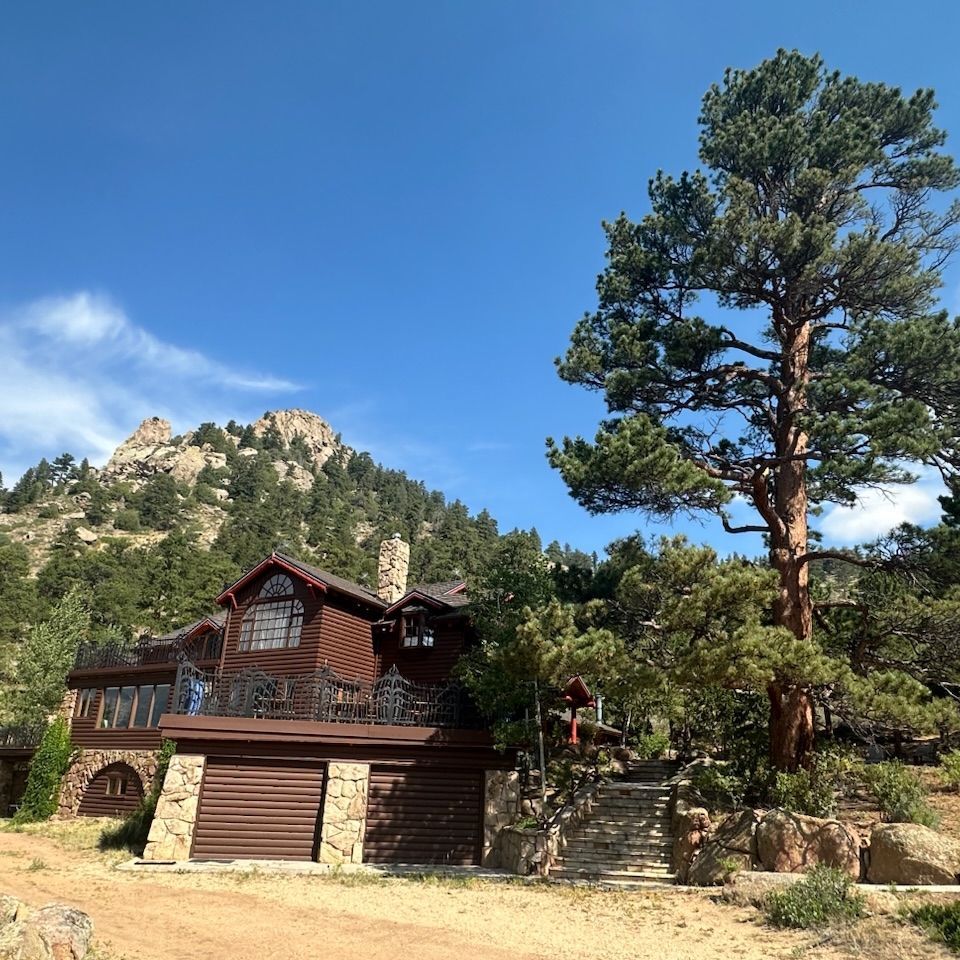 Rustic cabin among pine trees with rocky mountains and blue sky in the background