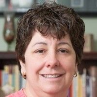 Close-up portrait of a smiling person with short brown hair, in front of bookshelves.