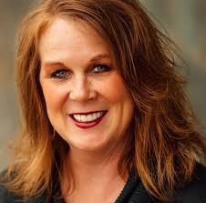 Smiling woman with wavy auburn hair against a blurred gray background