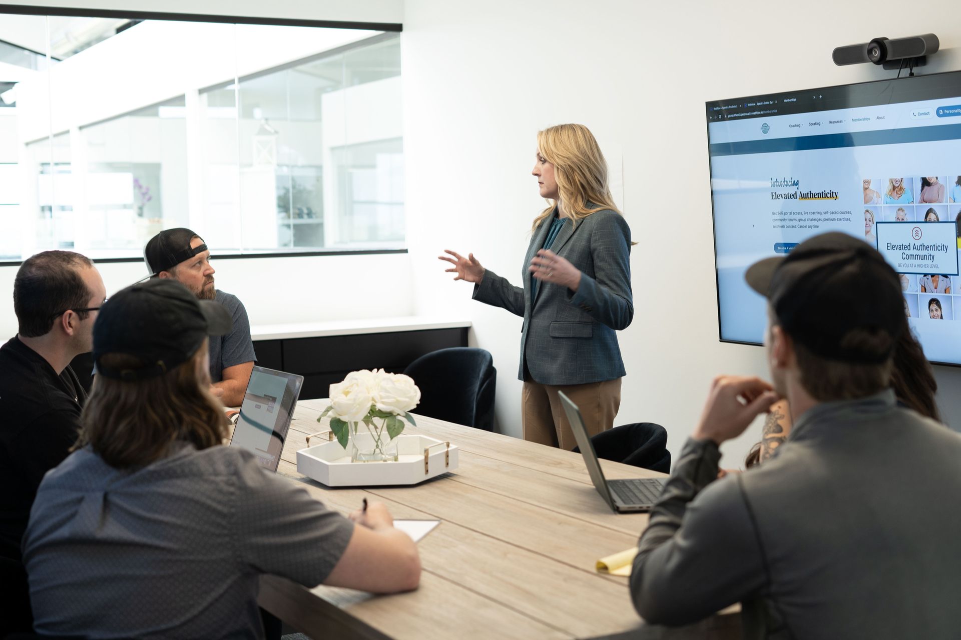 Business meeting with presenter beside a screen, speaking to colleagues around a conference table.