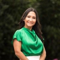 Woman in a bright green blouse smiling outdoors against a blurred dark background