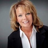 Smiling woman in a black blazer and white shirt against a gray studio background