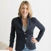 Smiling woman in a dark blazer standing indoors with one hand on her hip