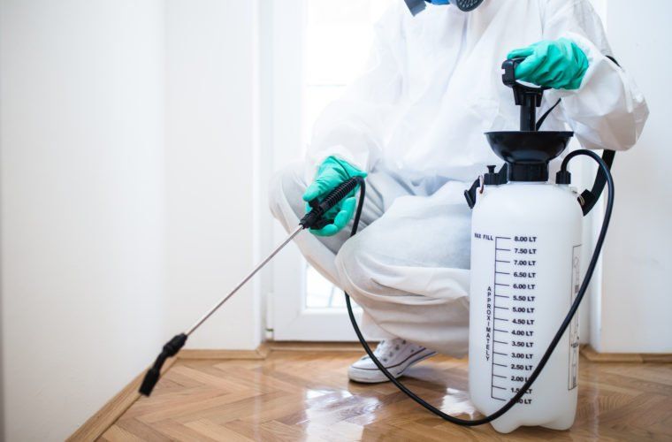 A man in a protective suit is spraying a room with a sprayer.