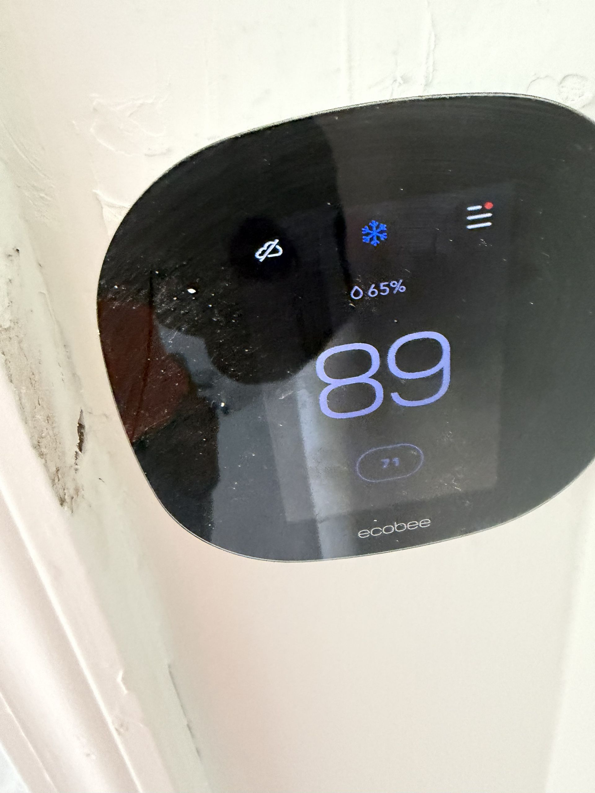 Close-up of a black digital thermostat on a white wall showing 89° and fan settings.