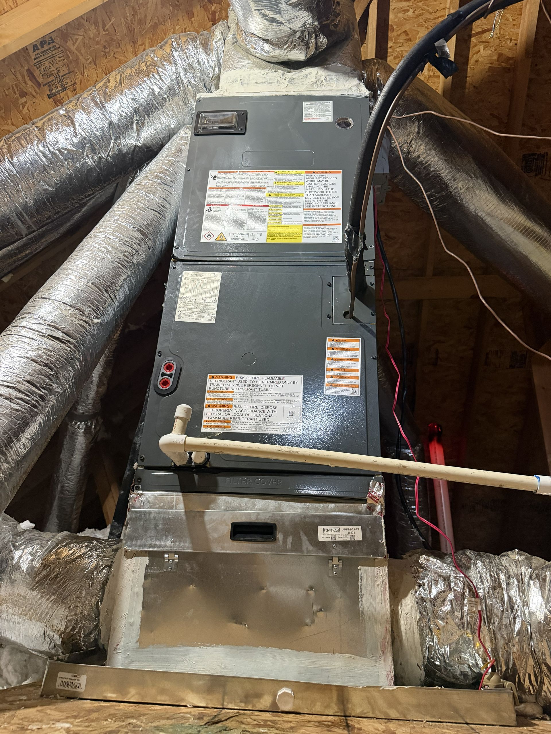 Furnace unit in insulated attic, surrounded by ductwork and foil-lined walls.