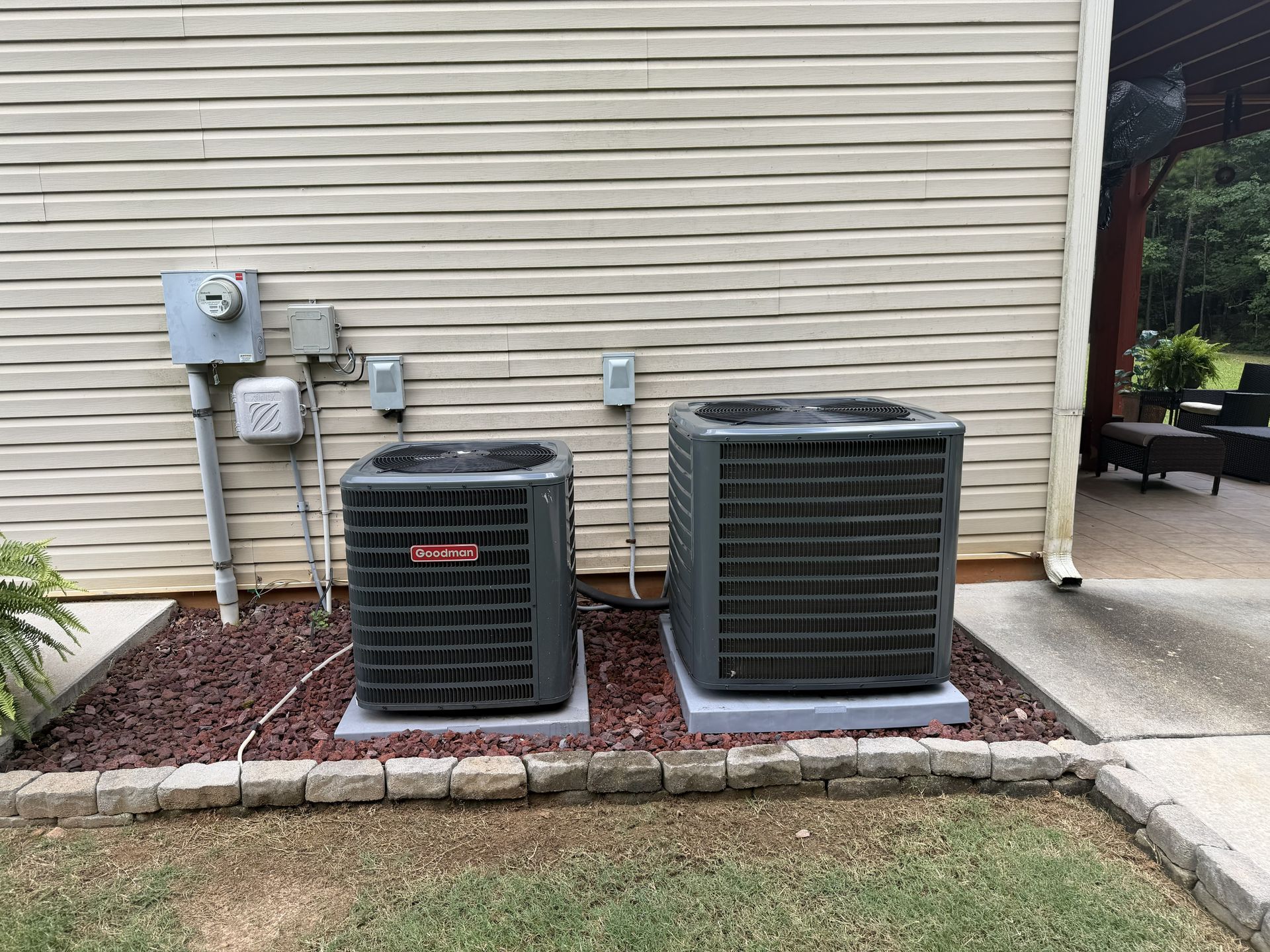 Two outdoor air conditioning units beside a beige house wall and utility meters