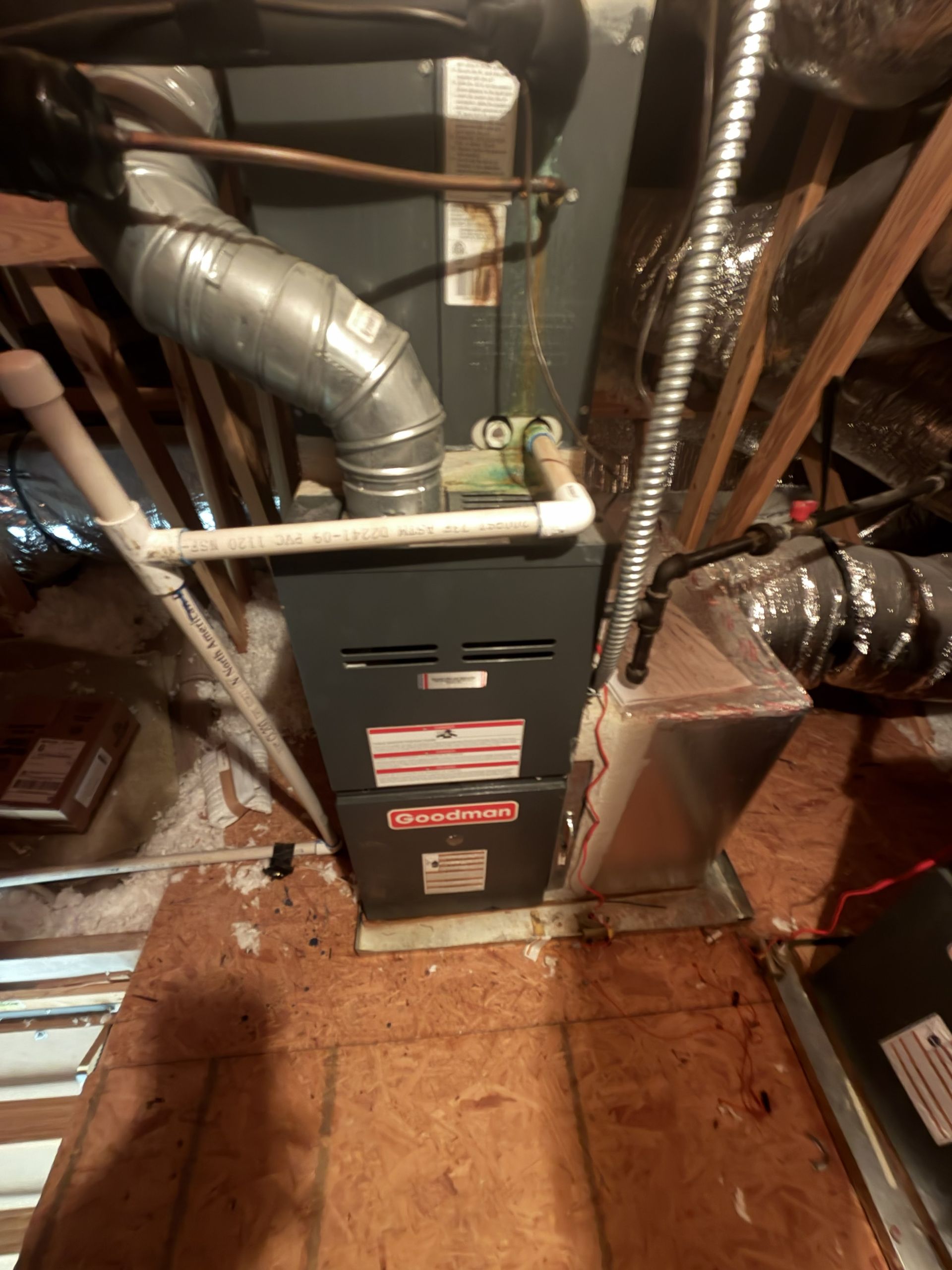 Basement furnace surrounded by silver ductwork and pipes on a wooden floor.