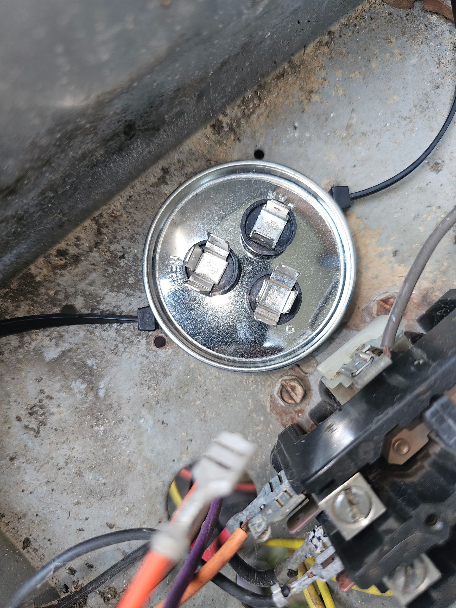 Round metal light fixture with exposed bulbs and wires on a concrete floor, next to mechanical parts