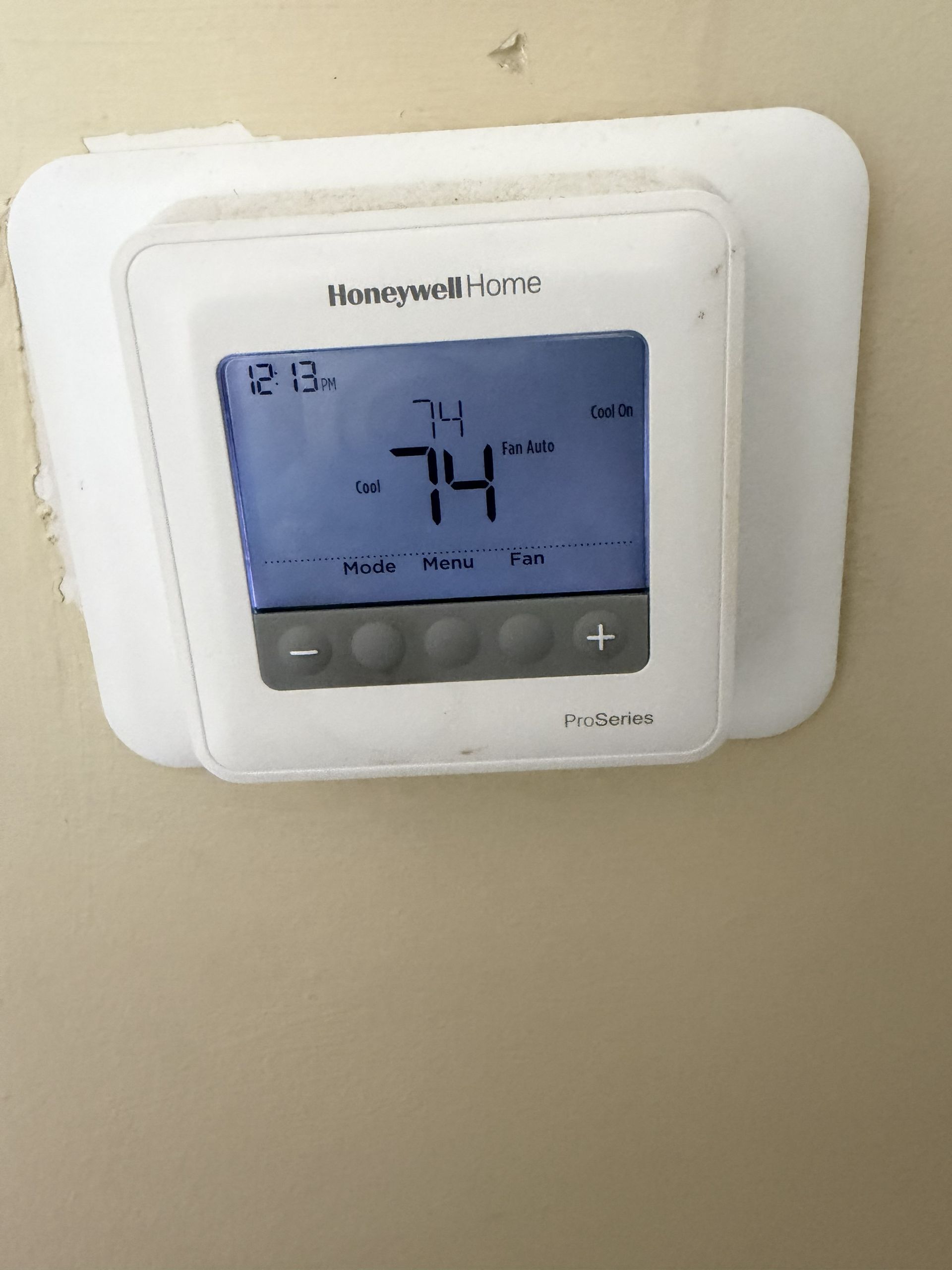 Honeywell thermostat mounted on a wall, displaying 74°F on a blue backlit screen