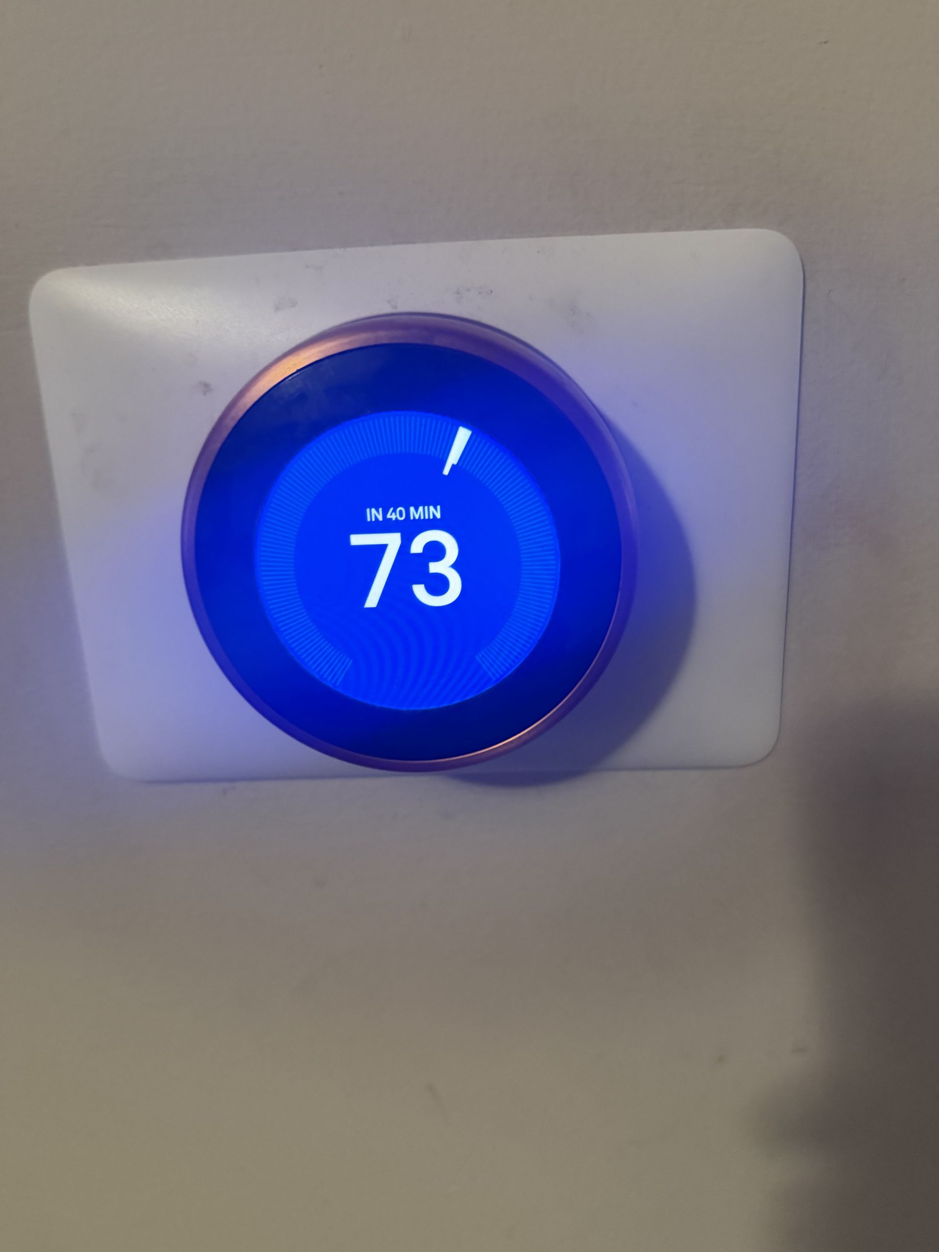 Blue smart thermostat on a wall displaying 73°F.