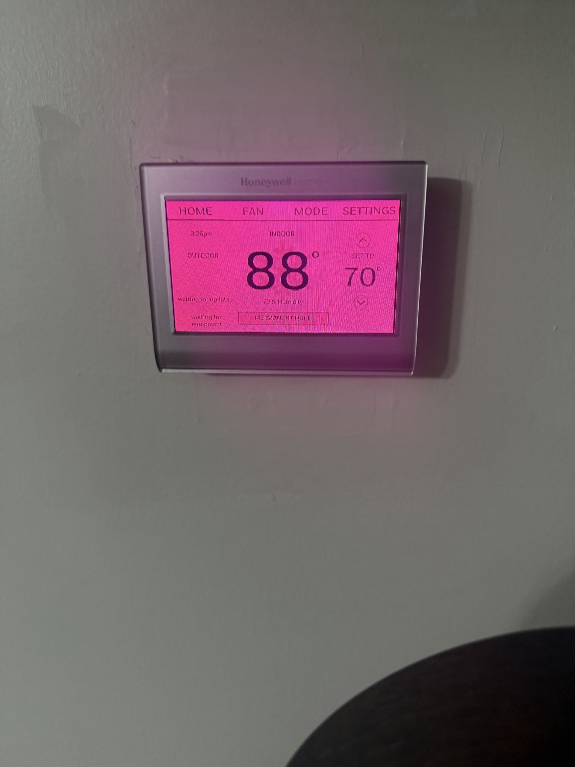 Pink digital thermostat display on a wall showing 88° with humidity reading 70%
